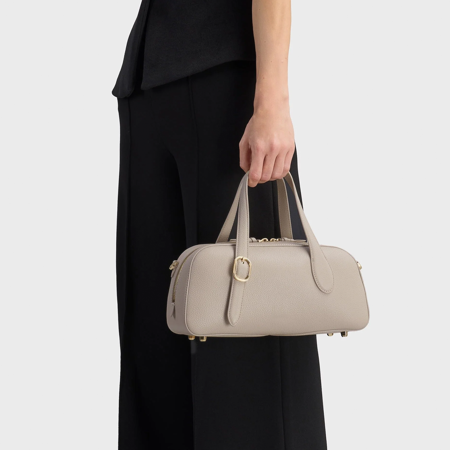 Calm Pale Ash Grey Compact Oval Barrel Carryall With Polished Golden Zipper Hardware And Base Protective Metal Studs